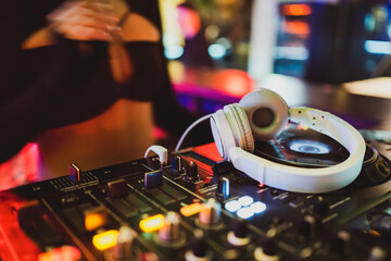 Professional DJ mixing console with white headphones resting on it, illuminated by colorful lights....