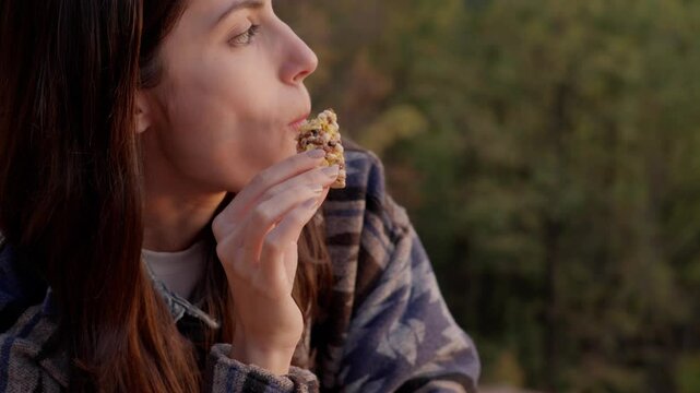 Female hiker enjoying protein bar while resting during woodland walk, golden sunlight filtering through trees during peaceful moment of mindful nutrition
