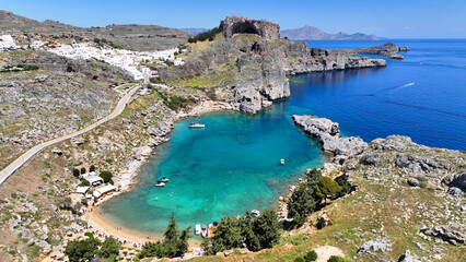 Aerial drone photo of stunning crystal clear sea and small organized beach of Saint Paul's bay overlooked by archaeological site of Acropolis of Lindos, Rhodes island, Dodecanese, Greece