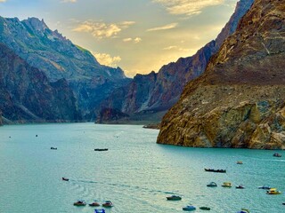 A breathtaking aerial view of colorful boats floating on the serene turquoise waters of Attabad Lake during sunset in Hunza Valley, Pakistan. 
