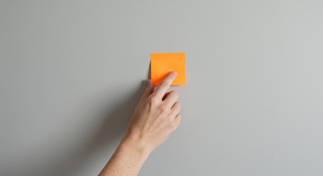 Hand placing orange sticky note on gray wall