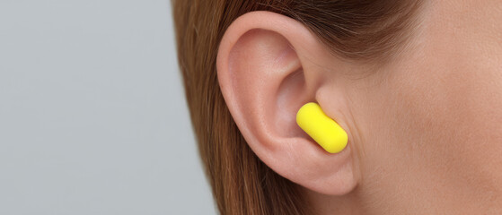 Ear with a yellow earplug inserted, close-up view. Concept: hearing protection, safety, listening