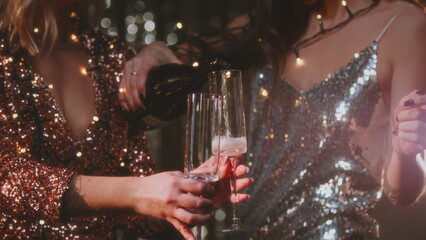The girls pour champagne into round glasses. Women in a sparkling dress, cocktail creamers, le coupe