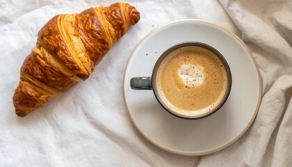 A simple breakfast with a cup of black coffee and a croissant on a crumpled white sheet.