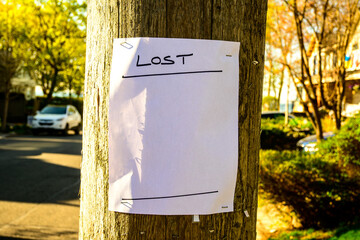 Blank lost  handbill stapled to a wooden utility pole out of focus street scene in background room...