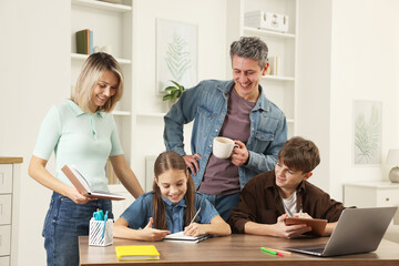 Happy parents and their children doing homework with laptop at table indoors