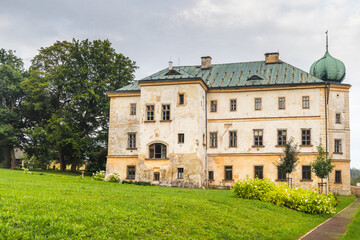 Fototapeta premium Adrspach castle in Adrspach-Teplice Rocks area, in Hradec Kralove Region in the Czech Republic, Europe. Exterior view of a historic building with a large green lawn, trees, and a cloudy sky overhead.