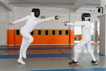 Female fencer leaping forward in attack during indoor match.