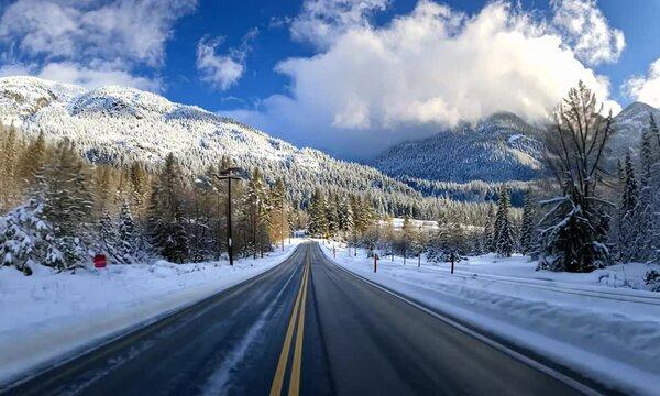 Snow-covered mountain road with pine trees under blue sky during winter day, representing travel, nature, and seasonal landscapes.