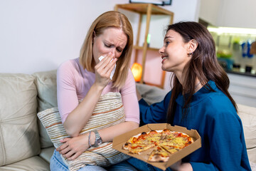 In a quiet living room, two best friends share a deeply emotional moment. One is crying while...
