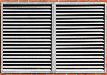 A gray metal grate covering a window in an orange brick wall
