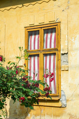 Romantic window of an old European house with red roses and vintage striped sunshade