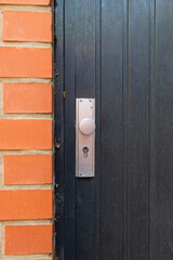 
Black closed door with keyhole and metal handle near the orange brick wall of the building