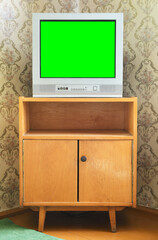 An old TV with a green screen on the nightstand against the background of wallpaper.