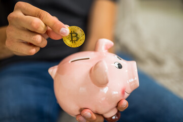 A young man places a bitcoin symbol or representation into a traditional piggy bank, merging modern...