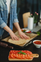 Cooking homemade pizza. Female hands making dough, adding sauce and ingredients.