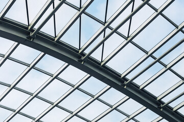 Modern glass roof with steel structure. Architectural ceiling in daylight. Transparent panels with grid lines. Urban construction with metal beams. Light geometric pattern in architecture.