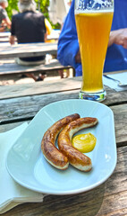 Bavarian grilled sausages - Bratwurst with mustard and  light frothy beer at beer garden, traditional meal