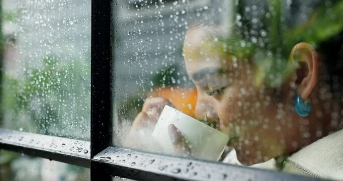 Woman, thinking and drinking coffee with window rain drops for winter season, cold weather or dream at home. Female person, relax and wonder with thought or mug for caffeine or condensation at house