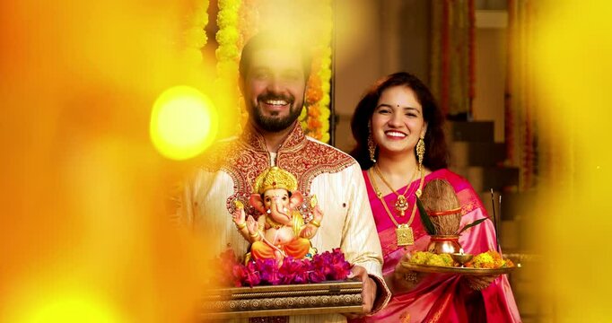 Indian Couple Welcoming Ganesh Idol with Joy, Young husband wife in Traditional Attire Holding Ganpati Bappa Idol, Puja Thali While Smiling and Chanting Bappa Morya During Ganesh Festival Celebration