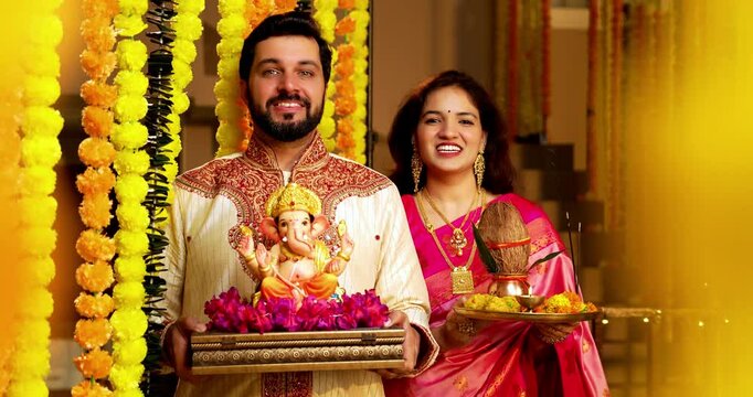 Indian Couple Welcoming Ganesh Idol with Joy, Young husband wife in Traditional Attire Holding Ganpati Bappa Idol, Puja Thali While Smiling and Chanting Bappa Morya During Ganesh Festival Celebration