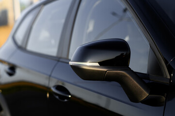 Black car parked in a city background in the setting sun. Close-up of the side mirror
