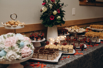A table with gourmet desserts at a wedding, decorated with floral arrangements and festive decor. The scene conveys attention to detail, hospitality and festive mood.