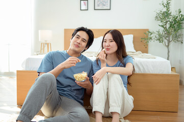 Couple Enjoying Popcorn Together While Sitting on the Floor in a Cozy Bedroom During the Afternoon