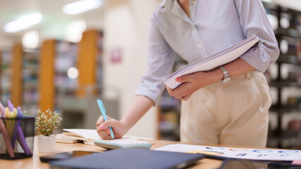 Asian Woman Studying Finance Chart Using Calculator for Business Accounting at Library Learning...