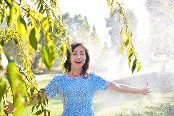 Joyful Young Woman Laughing Enjoying Refreshing Water Spray from Park Sprinklers