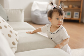 Fototapeta premium Cute Baby Girl Playing in Bright Living Room, Exploring Soft Couch and Modern Home Interior with Toys and Plush Furniture