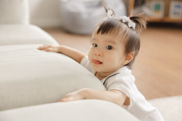 Cute toddler with playful expression exploring living room furniture and enjoying indoor playtime...