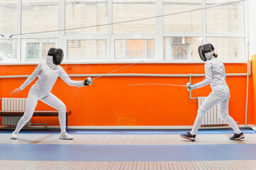 Female fencers preparing to attack in bright fencing hall.