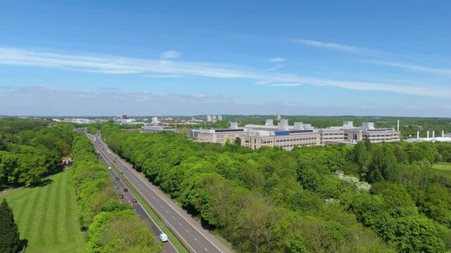 Aerial drone view motorway highway green lush forest GSK building manufacturing Stevenage Pharmaceuticals England UK sunny  