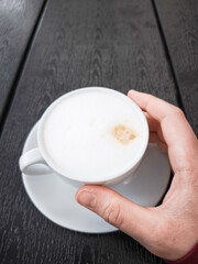 Creamy coffee cup Cappuccino held in hand on dark wooden table showcasing a delightful beverage concept. copy space