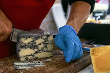 Seller slicing mold cheese on wooden board. Cheese shop.