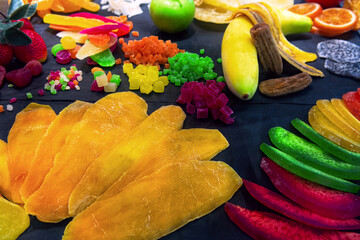 Various fruits (kiwi, mango, pineapple, papaya, banana, orange, lemon, apple, melon, dragon fruit) in display case of candy store. Dry fruits background.