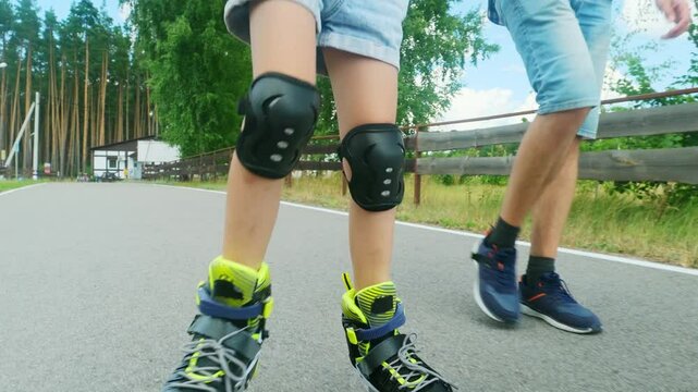 Child girl holding dad's hand, roller skating in the summer park.