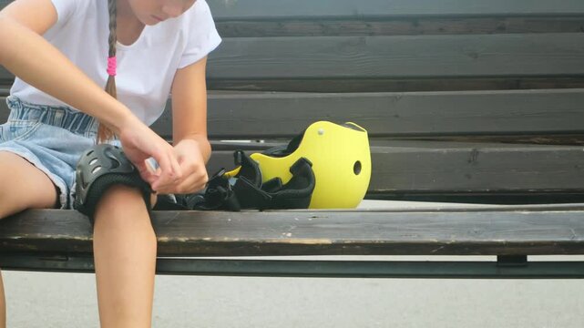 Young skater girl putting on protective shin guards and knee pads for skating. child rollerblader preparing for a ride in skatepark in summer
