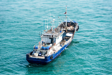 A blue and white fishing boat sails on a calm sea, with gentle waves. The vessel features a deck equipped with fishing gear and a visible wheelhouse. © Mariusz