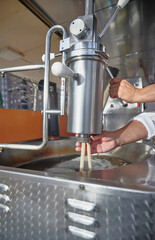 Unrecognizable man’s hands operating dough extruder and dispenser machine to fry churros in an industrial fryer. Manual process in churro preparation.
