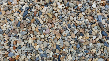 Close up of sea stones, river pebbles or rock pile background. Top view of many small stones in different colors. Abstract rough wallpaper concept about nature.