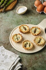 Shortcrust pastry tartlets with asparagus and cream filling on a ceramic plate on a green concrete background. Recipes asparagus.