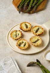 Shortcrust tartlets with asparagus and creamy filling on a ceramic plate on a light concrete background. Recipes asparagus.