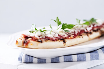 Open-faced toasted salami and cheese sandwich on bright background.	