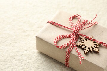 Gift wrapped in kraft paper with bow and ornament on white textured table, closeup. Space for text