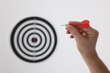Targeting. Man with arrow aiming at dart board on light background, closeup