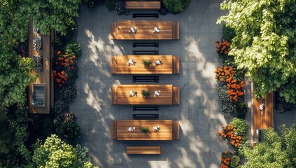 Elevated view of a landscaped outdoor dining area with long wooden tables and benches, surrounded by lush greenery and vibrant flowers.  A central paved area