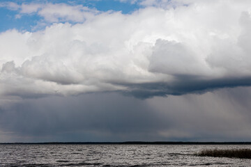 A dark storm approaches over a calm lake, with heavy rain visible on the horizon and dense clouds casting shadows across the sky and water ample copy space.