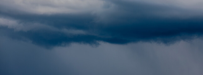 Fototapeta premium Thick storm clouds stretch across the sky with a visible curtain of rain falling below, creating a dramatic and moody atmosphere ample copy space.